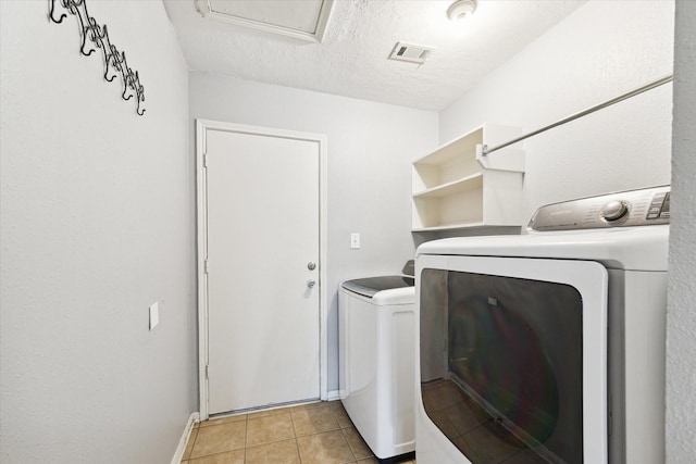 laundry room featuring separate washer and dryer, light tile patterned floors, and a textured ceiling