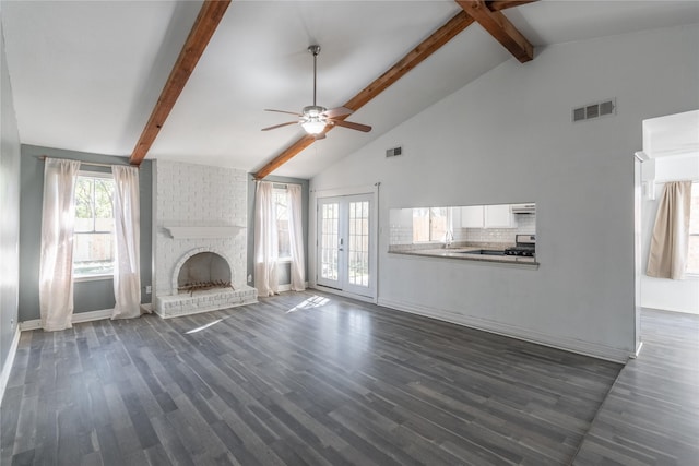 unfurnished living room with ceiling fan, french doors, sink, beamed ceiling, and a fireplace