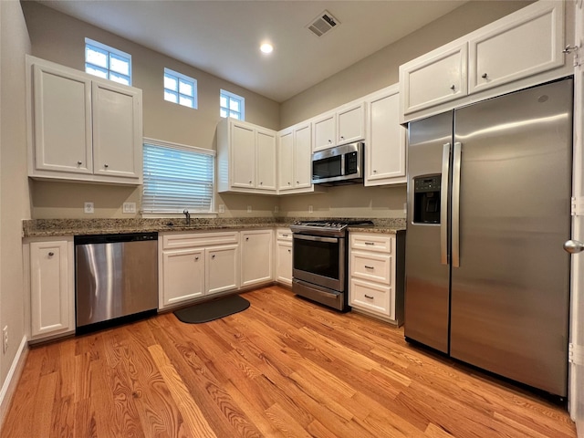 kitchen with white cabinets, light stone counters, stainless steel appliances, and light hardwood / wood-style flooring