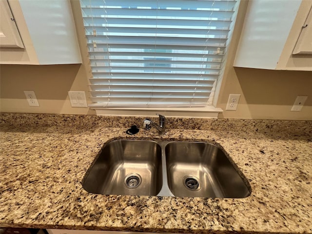 interior details featuring white cabinets, light stone counters, and sink