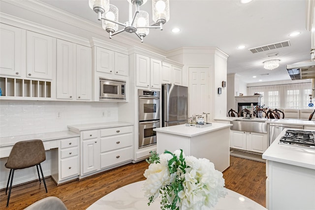 kitchen with decorative light fixtures, a kitchen island, white cabinetry, and appliances with stainless steel finishes