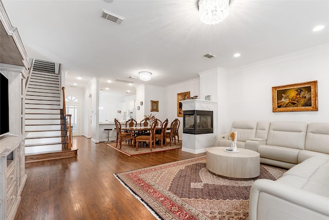 living room featuring a multi sided fireplace, dark hardwood / wood-style flooring, ornamental molding, and a notable chandelier