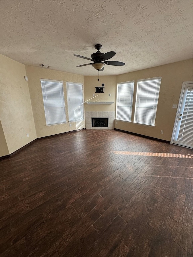 unfurnished living room featuring ceiling fan, a fireplace, dark wood-type flooring, and a textured ceiling