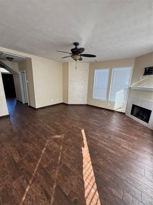 unfurnished living room featuring ceiling fan, dark hardwood / wood-style floors, a textured ceiling, and a tile fireplace