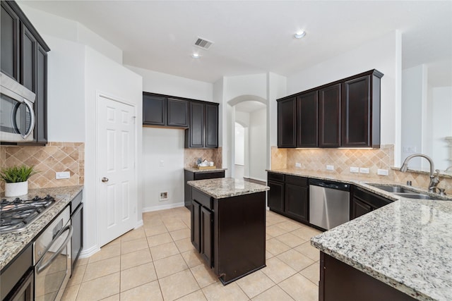 kitchen with sink, appliances with stainless steel finishes, a center island, light stone counters, and light tile patterned flooring