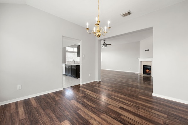 unfurnished dining area with ceiling fan with notable chandelier, sink, vaulted ceiling, dark hardwood / wood-style floors, and a tiled fireplace