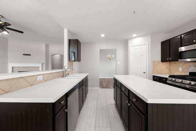 kitchen featuring ceiling fan with notable chandelier, sink, decorative backsplash, stainless steel appliances, and a tiled fireplace