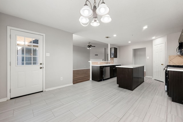 kitchen with pendant lighting, ceiling fan with notable chandelier, sink, appliances with stainless steel finishes, and a kitchen island