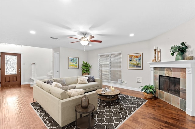 living room with wood-type flooring, ceiling fan, and a tiled fireplace