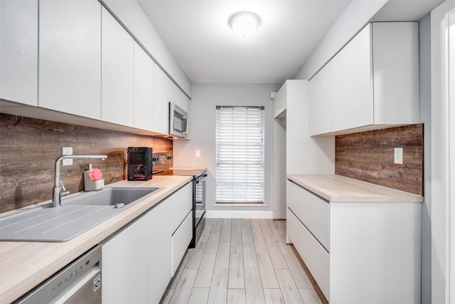 kitchen with sink, stainless steel appliances, tasteful backsplash, white cabinets, and light wood-type flooring