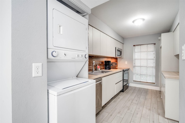 kitchen with decorative backsplash, stainless steel appliances, sink, stacked washer / dryer, and white cabinets