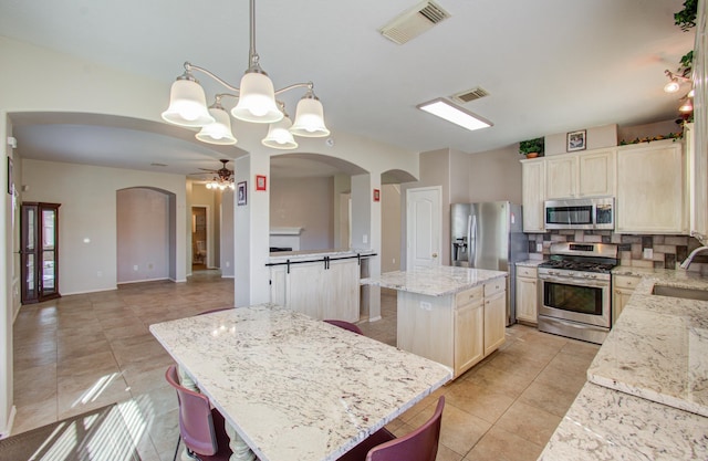 kitchen featuring appliances with stainless steel finishes, ceiling fan with notable chandelier, sink, a kitchen island, and hanging light fixtures