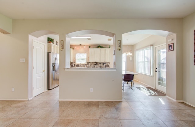 kitchen featuring decorative backsplash, stainless steel fridge, light tile patterned floors, and a notable chandelier