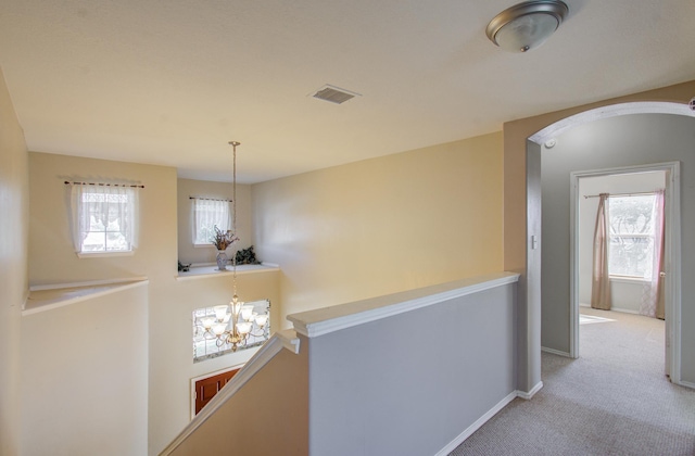 corridor featuring a notable chandelier, plenty of natural light, and light carpet