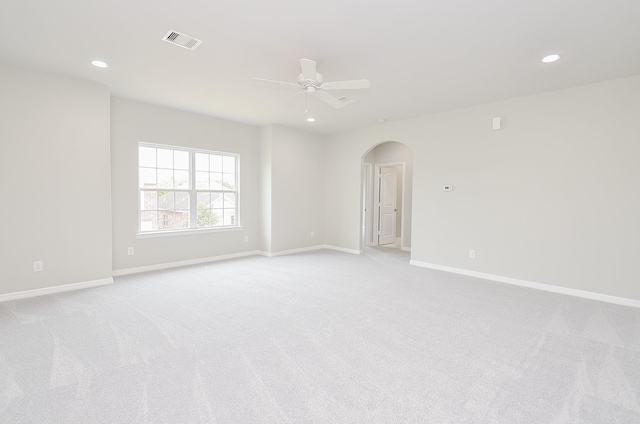 empty room with arched walkways, visible vents, a ceiling fan, light carpet, and baseboards