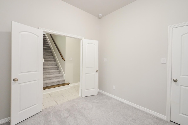 interior space featuring stairs, light tile patterned floors, baseboards, and light colored carpet