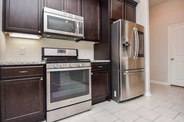 kitchen with light tile patterned floors, light stone counters, dark brown cabinets, appliances with stainless steel finishes, and tasteful backsplash