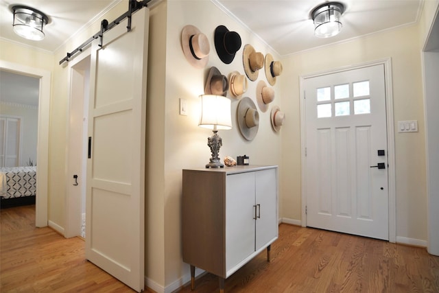 entryway with a barn door, ornamental molding, and light wood-type flooring