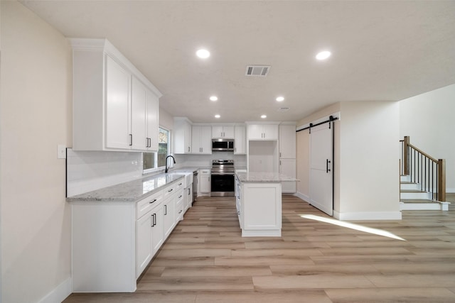 kitchen featuring a barn door, white cabinetry, a kitchen island, and appliances with stainless steel finishes