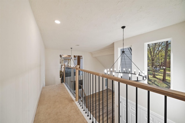 hall featuring a notable chandelier, a healthy amount of sunlight, carpet floors, and a textured ceiling