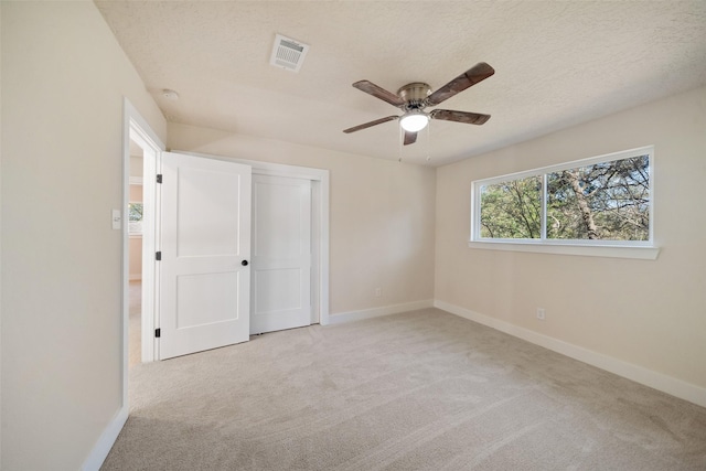 unfurnished bedroom with ceiling fan, light colored carpet, a textured ceiling, and a closet