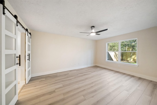 spare room with a textured ceiling, a barn door, light hardwood / wood-style floors, and ceiling fan