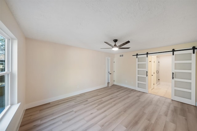 spare room with ceiling fan, a barn door, light wood-type flooring, and a textured ceiling