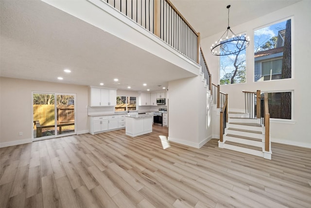 unfurnished living room with light wood-type flooring, a towering ceiling, and a chandelier