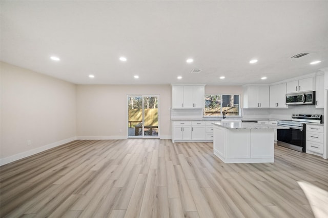 kitchen featuring light stone countertops, white cabinets, appliances with stainless steel finishes, a kitchen island, and light wood-type flooring