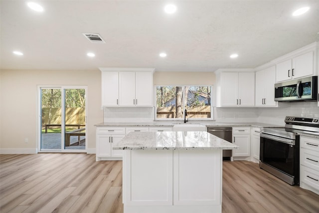 kitchen with light stone countertops, appliances with stainless steel finishes, sink, white cabinets, and a center island