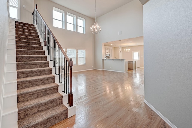 staircase featuring a wealth of natural light, hardwood / wood-style floors, a high ceiling, and an inviting chandelier