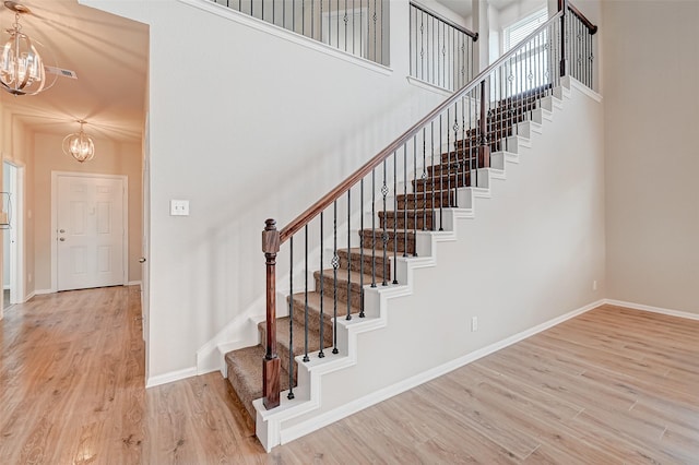 stairs with a high ceiling, an inviting chandelier, and hardwood / wood-style floors