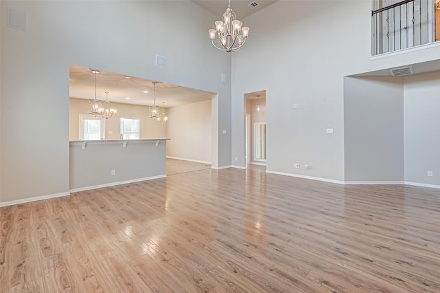 unfurnished living room featuring an inviting chandelier, a towering ceiling, and light wood-type flooring