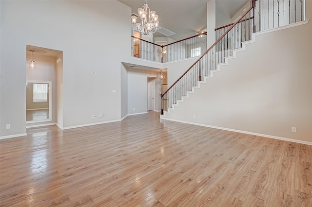 unfurnished living room featuring a towering ceiling, light hardwood / wood-style floors, and an inviting chandelier