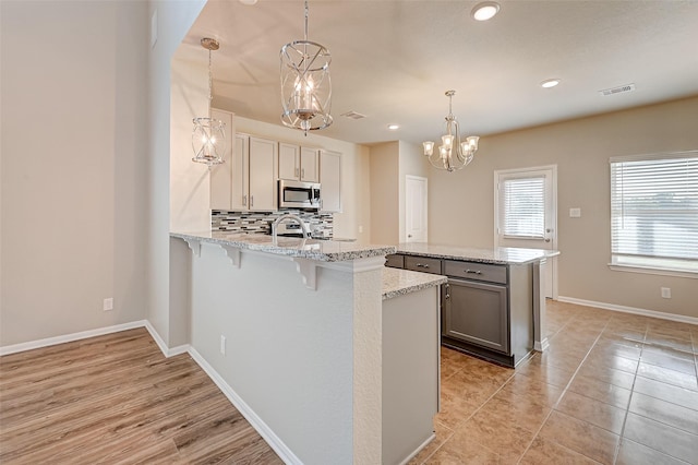 kitchen with pendant lighting, backsplash, light stone countertops, a kitchen bar, and stainless steel appliances