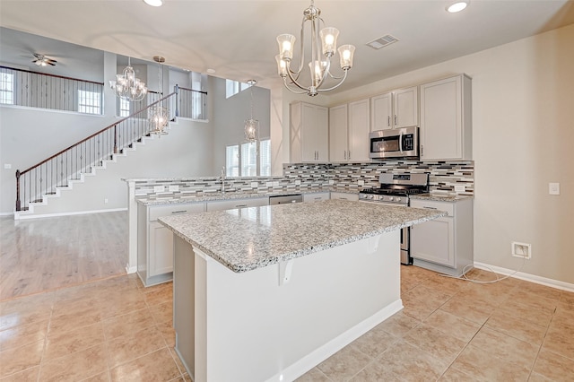 kitchen with ceiling fan, a kitchen island, light tile patterned floors, and appliances with stainless steel finishes