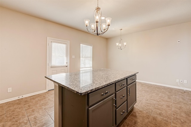 kitchen with dark brown cabinetry, light stone countertops, pendant lighting, a chandelier, and a kitchen island