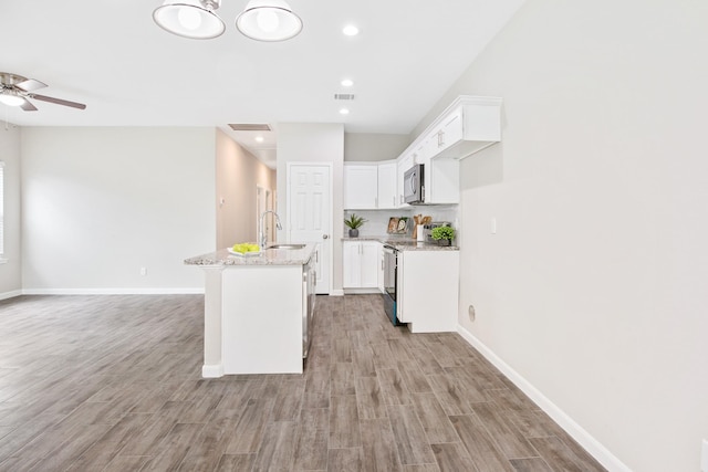 kitchen featuring light stone countertops, a kitchen island with sink, sink, electric stove, and white cabinetry