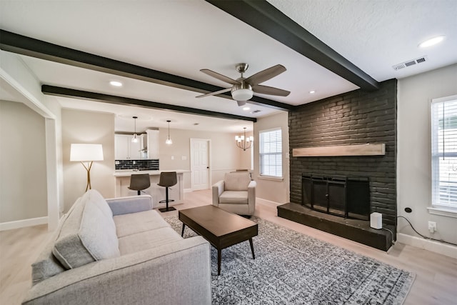 living room featuring beamed ceiling, ceiling fan with notable chandelier, light hardwood / wood-style flooring, and a brick fireplace