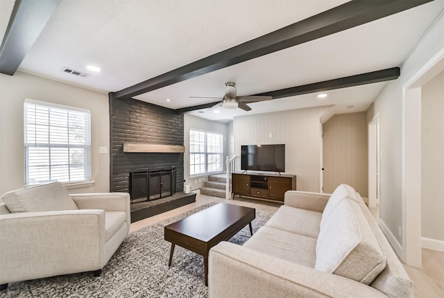 living room featuring a fireplace, light hardwood / wood-style floors, ceiling fan, and beamed ceiling