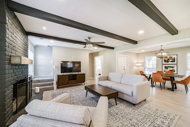 living room with beamed ceiling, ceiling fan with notable chandelier, hardwood / wood-style floors, and a brick fireplace