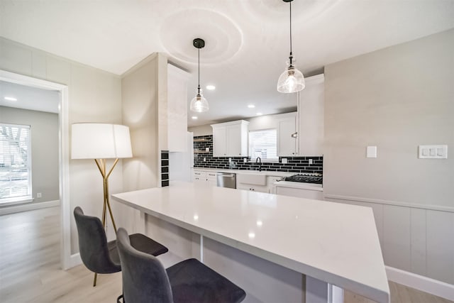 kitchen featuring pendant lighting, dishwasher, white cabinets, sink, and light hardwood / wood-style flooring