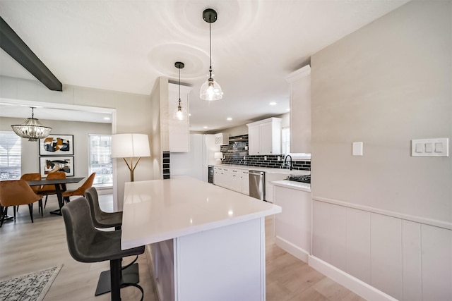 kitchen with white cabinets, stainless steel dishwasher, light hardwood / wood-style floors, decorative light fixtures, and beam ceiling