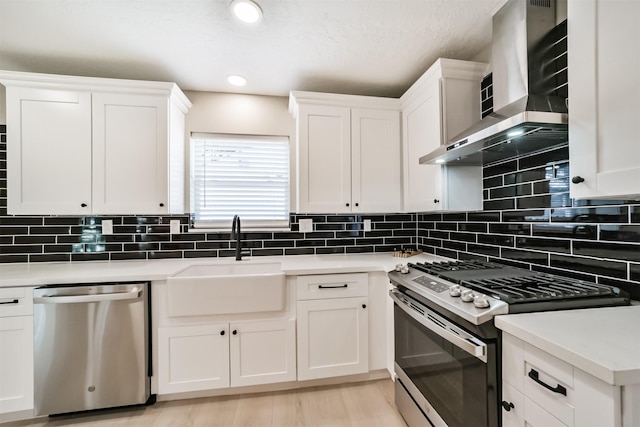 kitchen with sink, stainless steel appliances, wall chimney range hood, decorative backsplash, and white cabinets