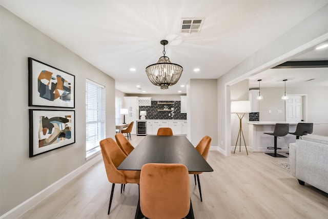 dining room with light hardwood / wood-style floors, an inviting chandelier, and beverage cooler