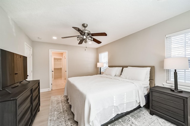 bedroom with ceiling fan, a spacious closet, multiple windows, light hardwood / wood-style floors, and a closet