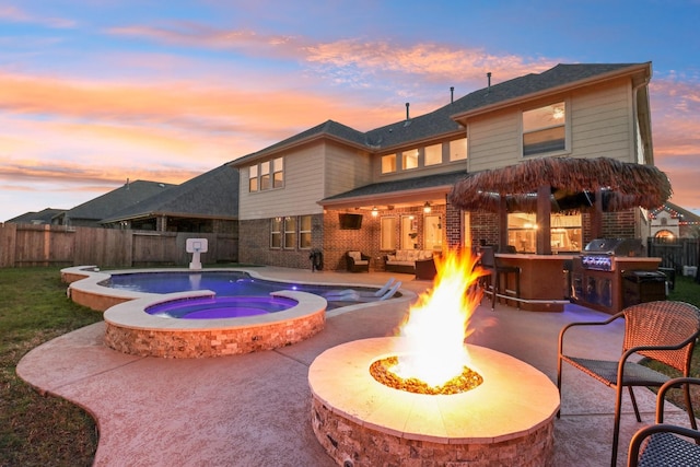 pool at dusk with exterior kitchen, grilling area, an outdoor living space with a fire pit, an in ground hot tub, and a patio