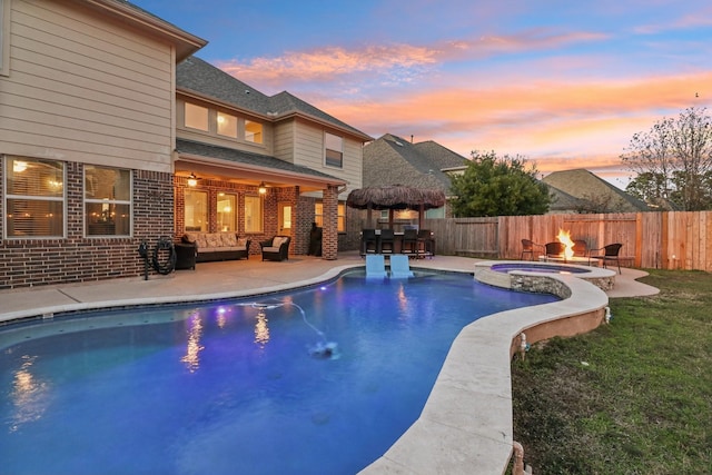 pool at dusk featuring a patio area, an in ground hot tub, a bar, and an outdoor living space with a fire pit