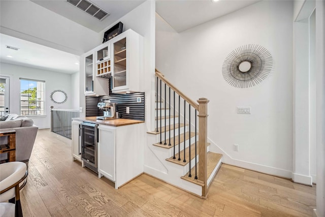 kitchen with wine cooler, white cabinetry, light hardwood / wood-style flooring, and butcher block counters