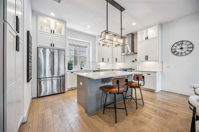 kitchen featuring white cabinetry, stainless steel fridge, a center island, and wall chimney range hood